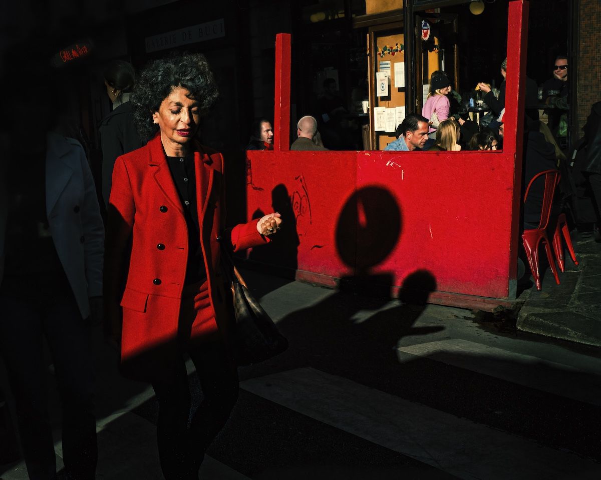 women in re jacket walking past restaurant with red front wall